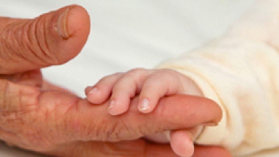 Eine Baby-Hand hält den Finger einer alten Person fest.